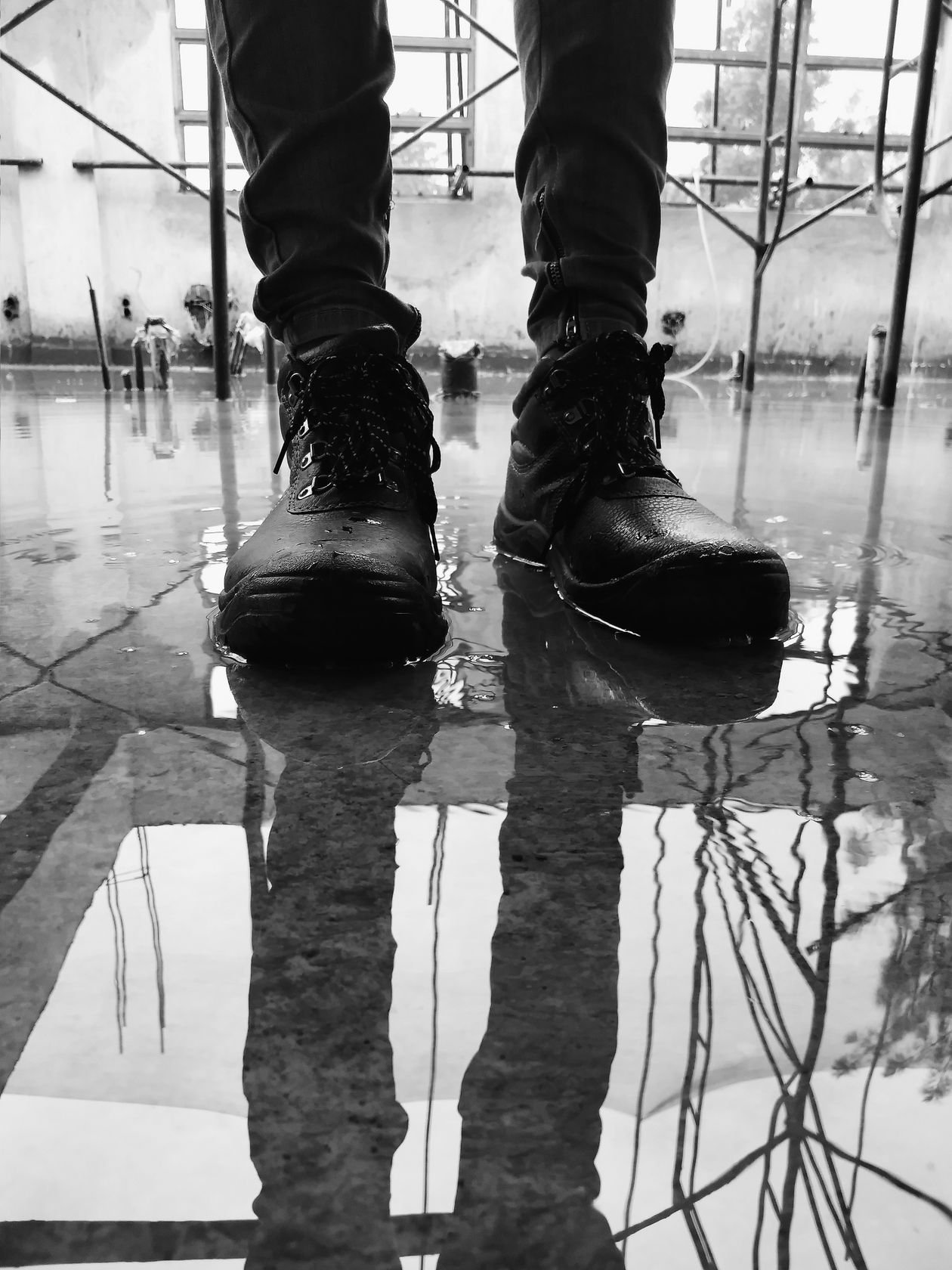 Close-up of black steel toe cap trainers standing in a reflective puddle
