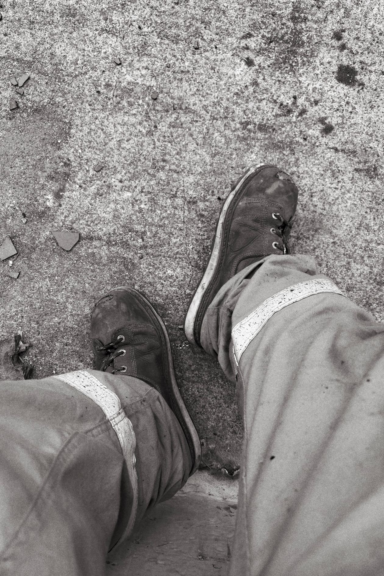 Worn work boots with protective toe caps on weathered concrete, seen from above